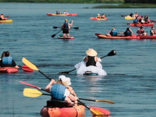 Cilvēki ar laivām un sup dēļiem peld ūdenī.